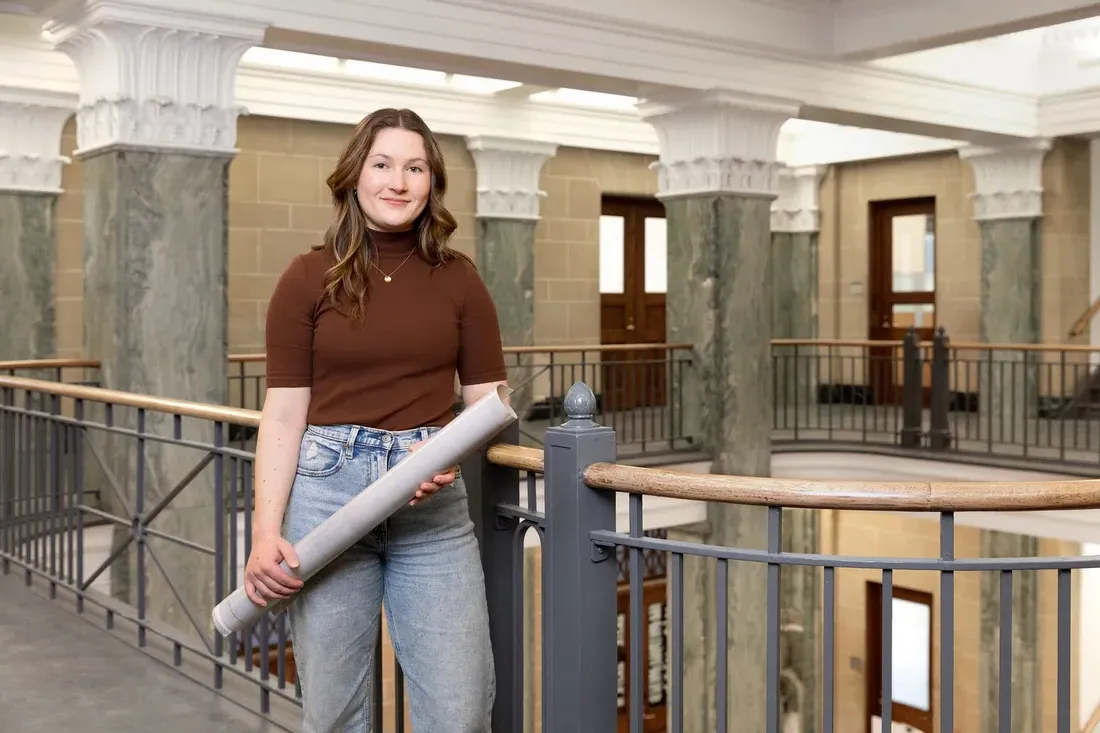 Student holds blueprints rolled up.